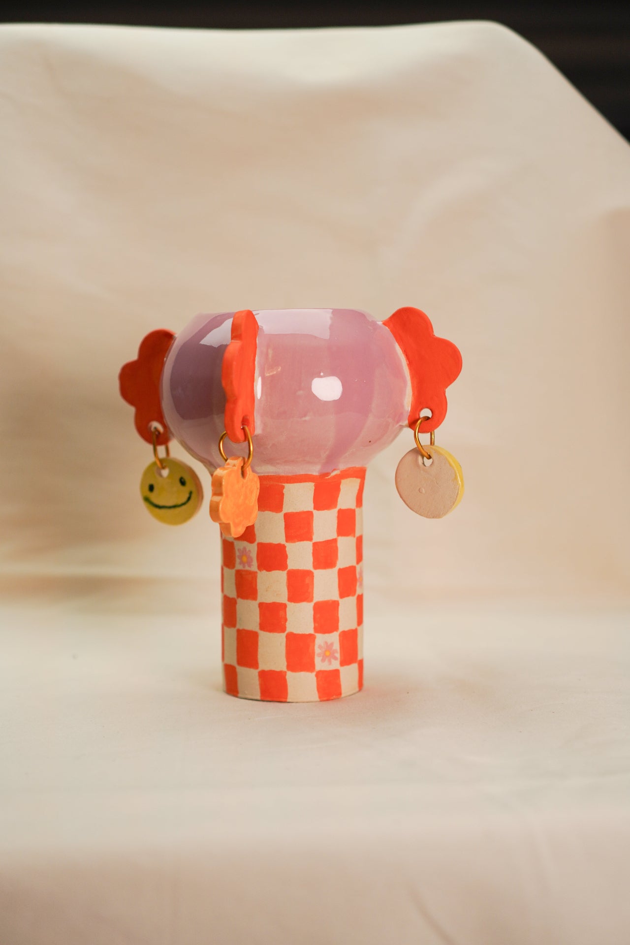 Ceramiczny wazon w kratkę różowo-pomarańczowy z zawieszkami w uśmiechy i kwiatki.